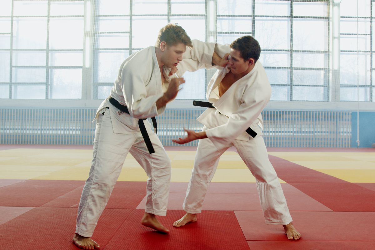 Two judo practitioners in white judogis practicing grappling techniques on a dojo mat